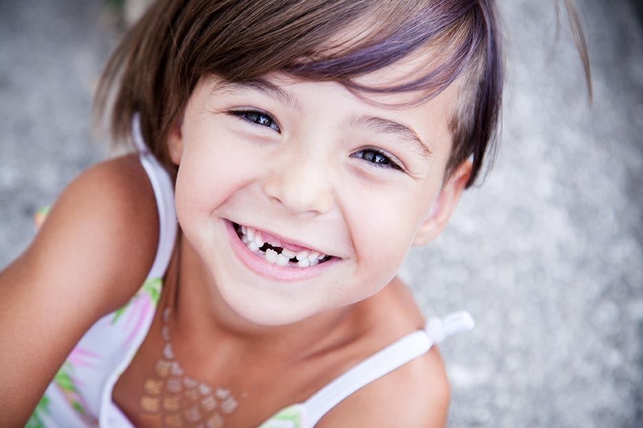 A young girl missing her baby teeth smiles widely.